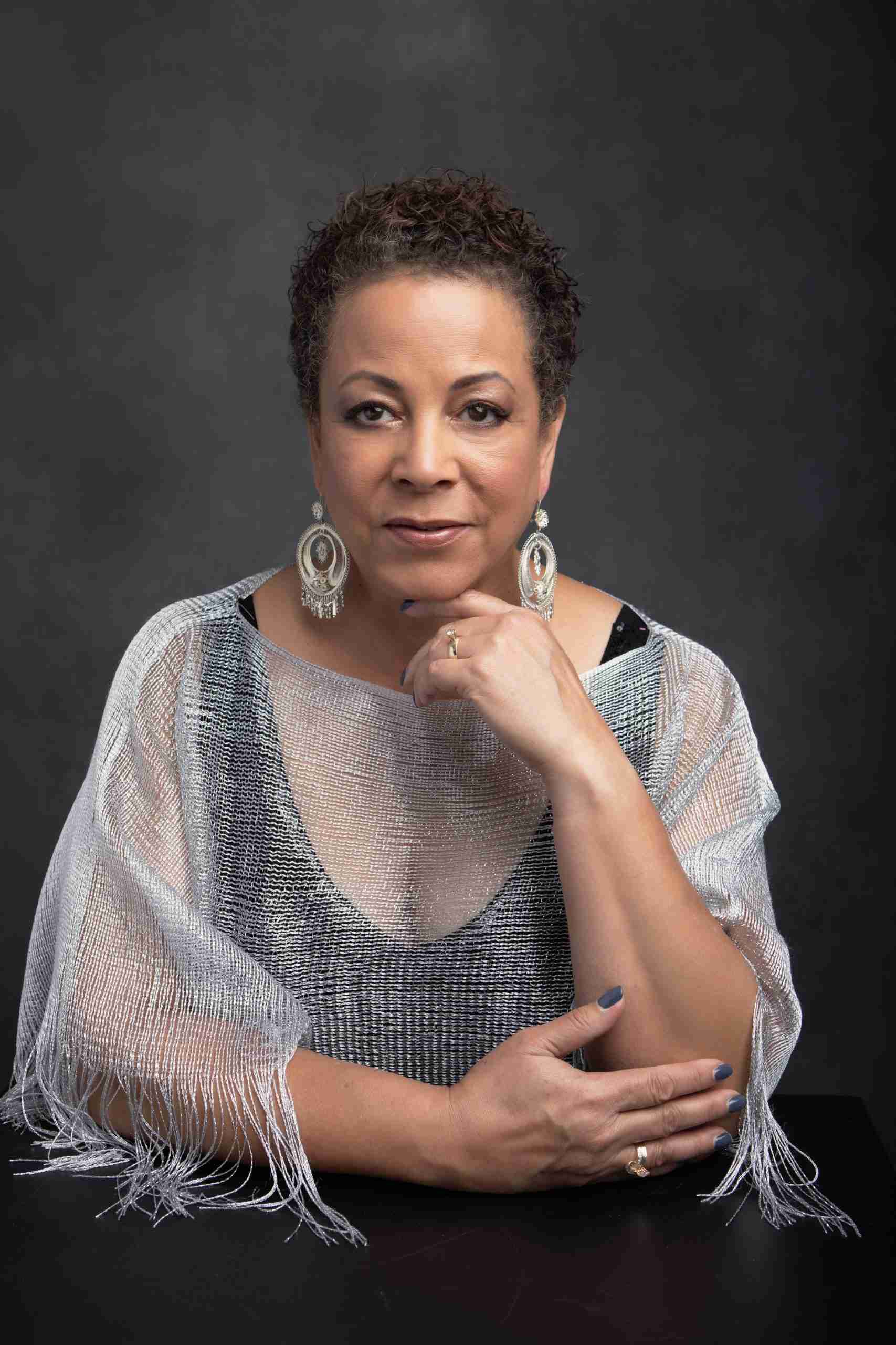 Woman in a silver wrap and statement earrings poses confidently against a charcoal backdrop.